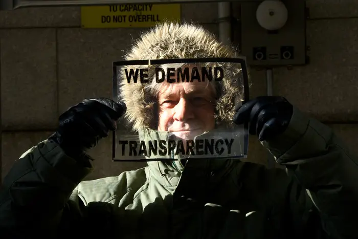 a guy holds up a translucent sign that reads "we demand transparency"